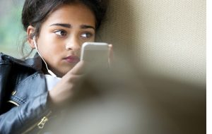 Young girl early teens playing on her phone and listening to music wearing headphones