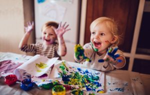 Nursery age kids painting at a table with teacher who has a early years certificate