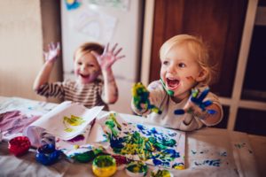 Nursery age kids painting at a table with teacher who has a early years certificate