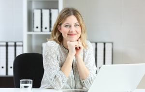 Front view portrait of a businesswoman posing looking at you on a desk at office