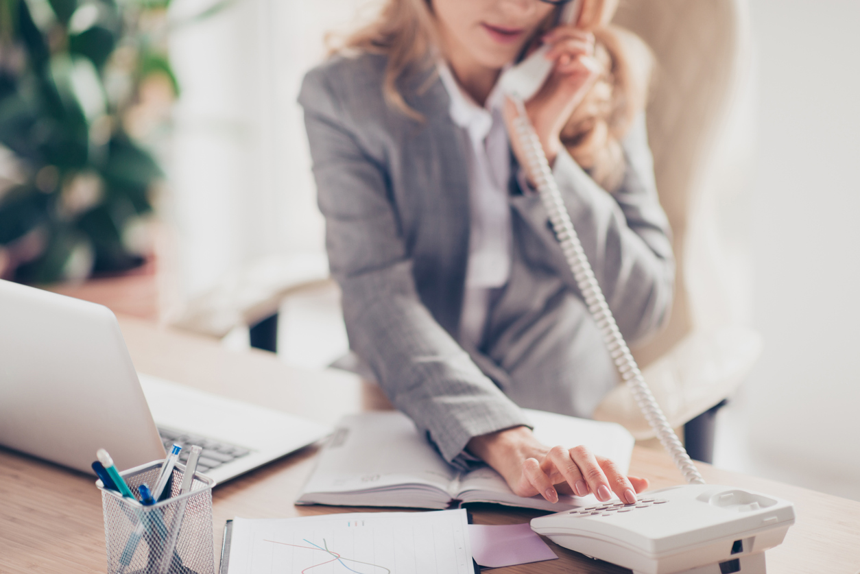 Cropped closeup photo of clever smart professional polite secretary in grey formal suit is calling to her boss, she is sitting at the table in office